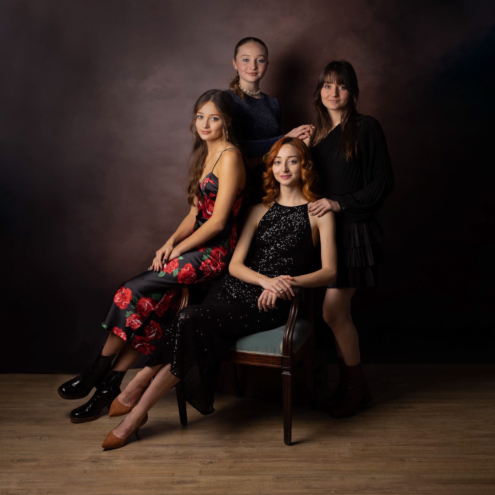 Portrait artistique de quatre sœurs élégantes en tenues de soirée dans un studio de photographie professionnel aux tons sombres.